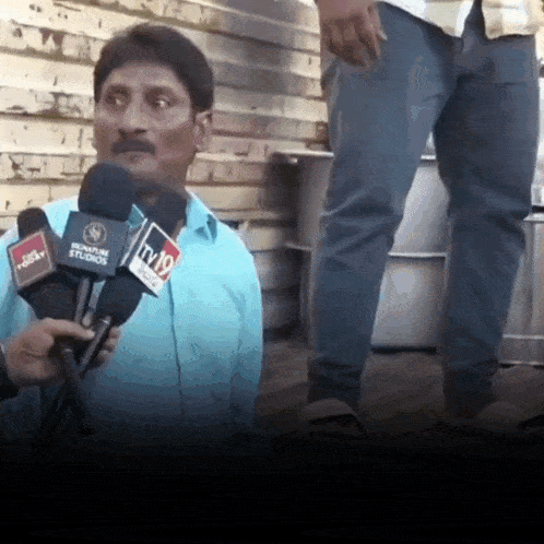 a man in a blue shirt is being interviewed by two microphones one of which says signature studios
