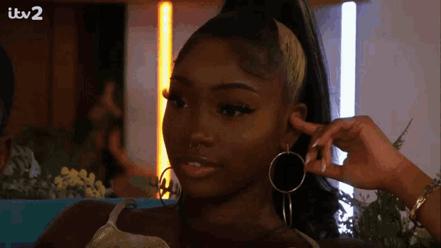 a woman wearing hoop earrings and a ponytail has itv 2 written on the bottom right