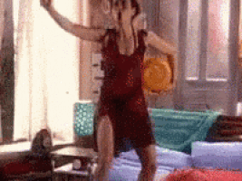 a woman in a red dress is dancing in a living room with her arms in the air .