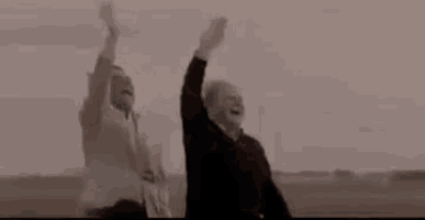 a man and a woman are standing next to each other with their arms up in the air .
