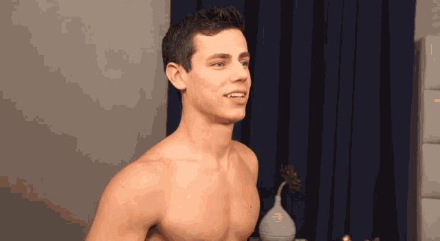 a shirtless man is standing in front of a blue curtain and smiling