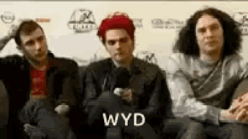 three men are sitting next to each other on a couch and one of them is holding a microphone .