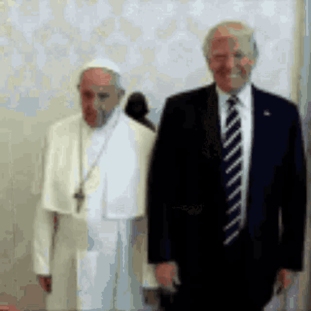 a man in a suit stands next to a man in a white robe .
