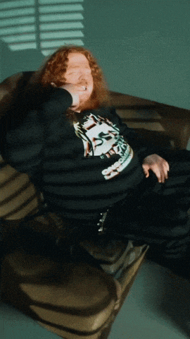 a man with red hair is laying on a couch wearing a shirt that says ' t.t. '
