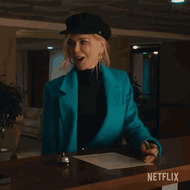 a woman in a blue jacket and black hat is sitting at a desk with a netflix sign on it