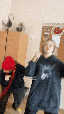 a blurry picture of two people dancing in a room with one wearing a red hat and the other wearing a black sweatshirt