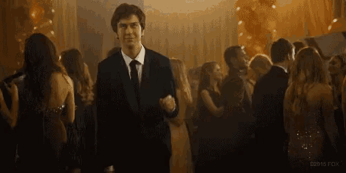 a man in a suit and tie is standing in front of a crowd of people at a prom .