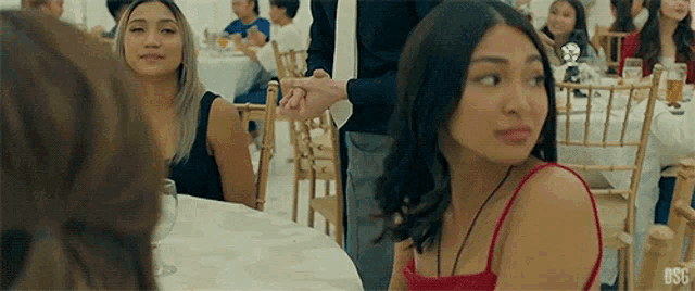 a woman in a red dress is holding a man 's hand while sitting at a table .