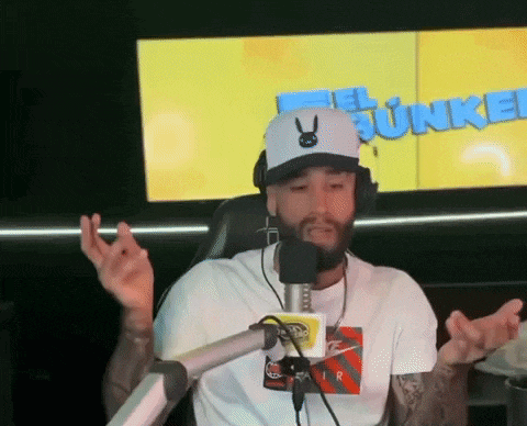 a man wearing a hat and headphones talks into a microphone in front of a screen that says el junkie