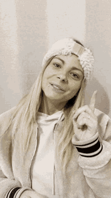 a woman wearing a headband and a jacket is pointing up with her fingers .