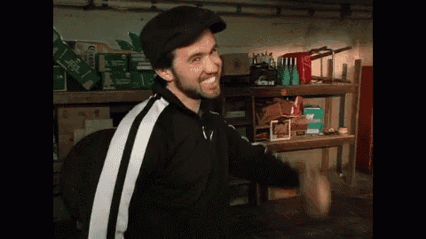 a man with a beard wearing a black hat and a black and white tracksuit is standing in a garage .