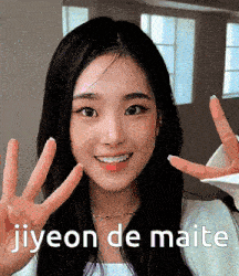 a woman is smiling and making a peace sign with her hands and the words jiyeon de maite below her .