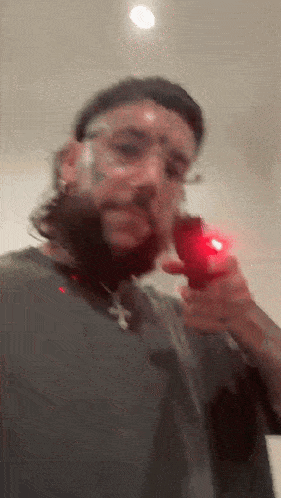 a man with a beard and glasses is holding a red object in his right hand .