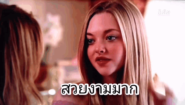 a woman with long blonde hair is looking at herself in a mirror and talking to another woman .