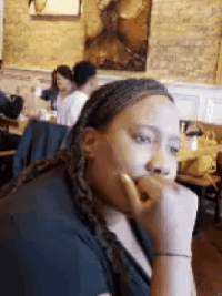 a woman with dreadlocks is sitting at a table in a restaurant with her hand on her chin .