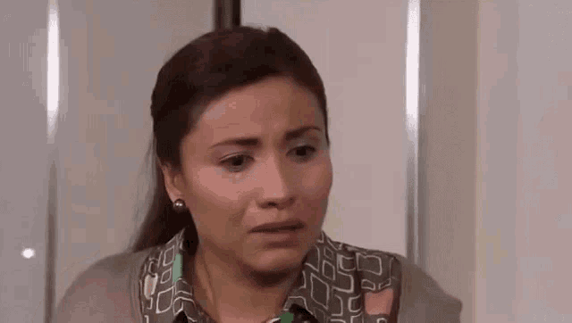 a woman is making a sad face while sitting in front of a white wall .