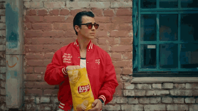 a man wearing a red jacket holds a bag of lays chips