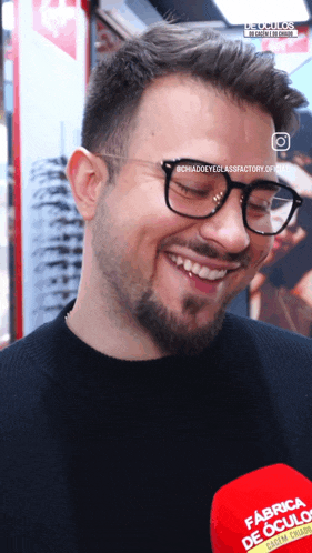 a man wearing glasses is smiling in front of a red microphone that says fabrica de culos