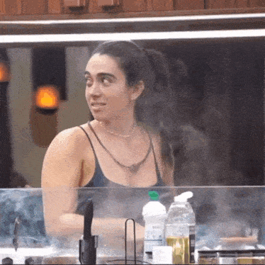 a woman in a black tank top is standing in front of a counter with cleaning supplies .
