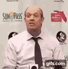a man in a white shirt and black tie is holding a microphone and making a funny face .