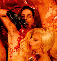 a woman laying next to a bloody man with a glove in his mouth