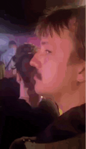 a man with a mustache is sitting in a crowd of people at a party .