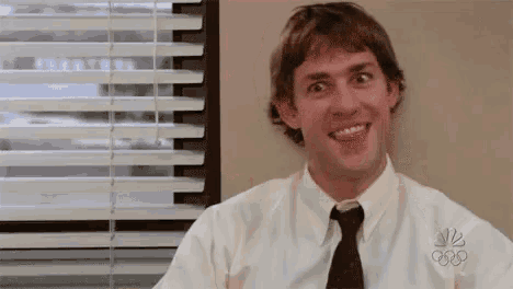 a man in a white shirt and tie is sitting in front of a window with blinds .