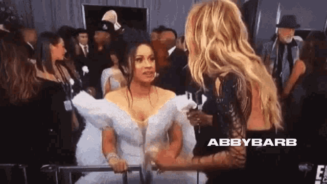 a woman in a white dress is talking to another woman in a black dress in a crowd .