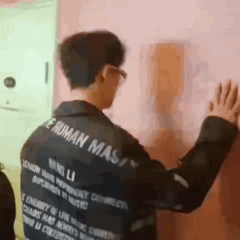 a man in a black jacket is standing next to a wall .