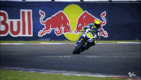 a person riding a motorcycle on a track with a red bull sign in the background