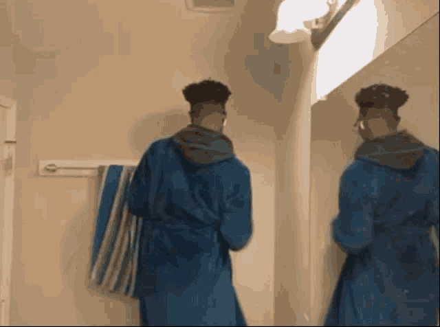 a man in a blue robe is looking at himself in the mirror .