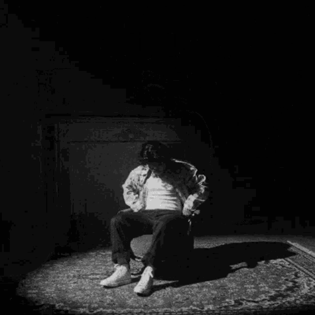 a black and white photo of a man sitting in a chair in a dark room