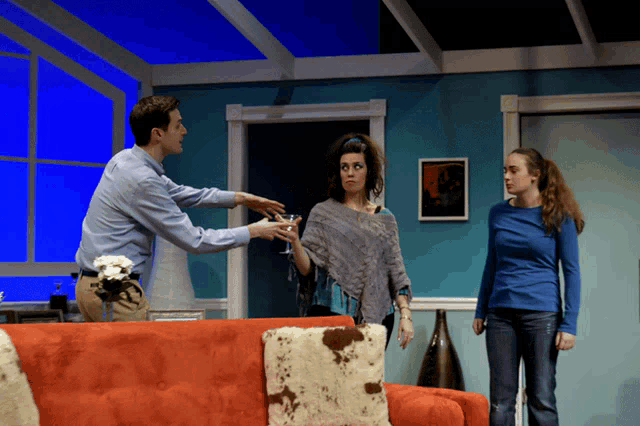 a man and two women are standing in a living room with a red couch