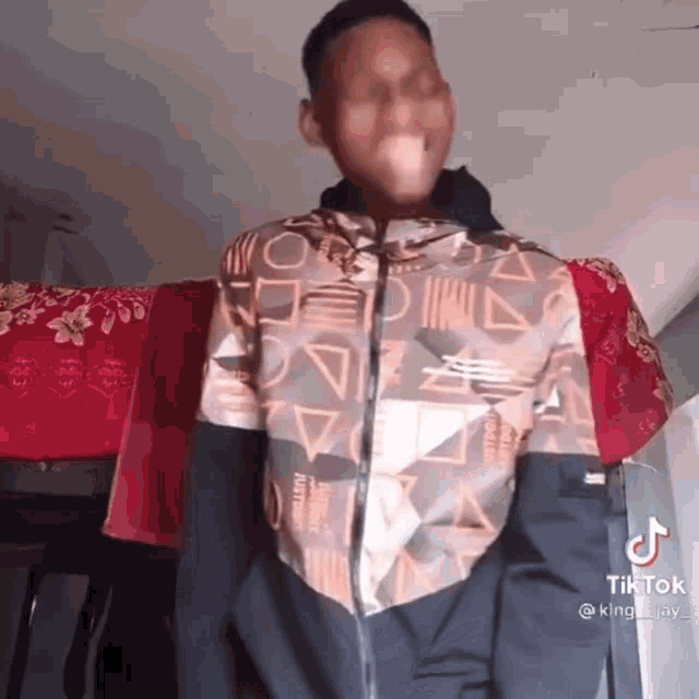 a young man wearing a jacket with a pattern on it is standing in a room .