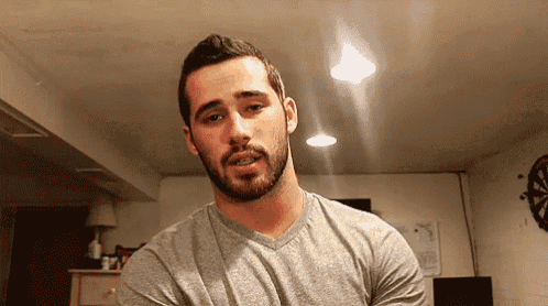 a man with a beard is wearing a grey shirt in a room
