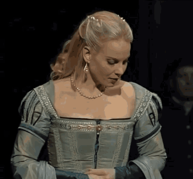 a woman wearing a blue dress and a pearl necklace looks down