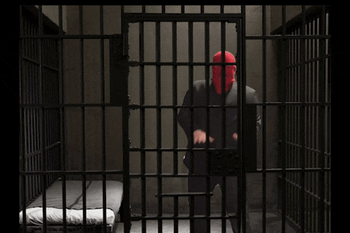a man in a red mask stands in a prison cell