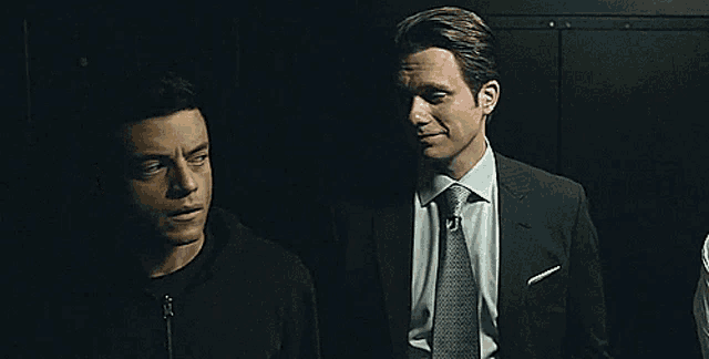 two men in suits are standing next to each other in the dark .