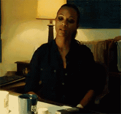 a woman in a black shirt sits at a table with a cup of coffee