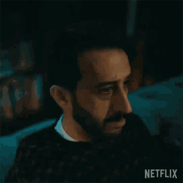 a man with a beard is looking at the camera in a dark room with a netflix logo in the corner .