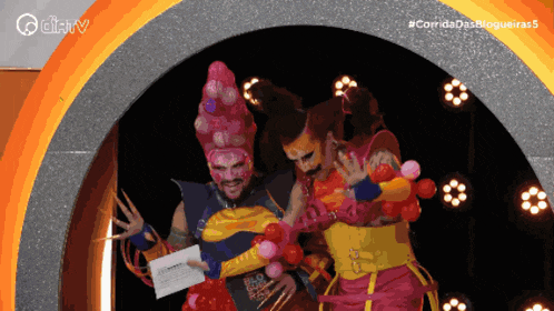two people in colorful costumes are standing in front of a sign that says " corrida das blogueiras "