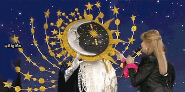 a woman is holding a microphone while standing next to a statue of the sun and moon