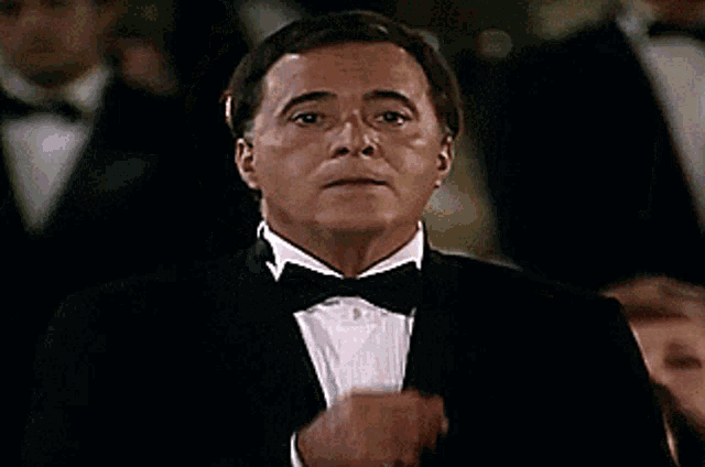 a man in a tuxedo and bow tie holds his fist up