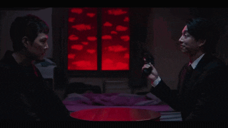 a man in a suit and tie is holding a gun and pointing it at another man .