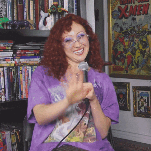a woman in a purple shirt is holding a microphone in front of a poster for daredevil xmen