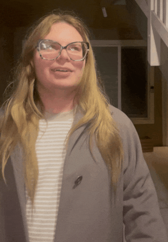 a woman wearing glasses and a grey jacket smiles