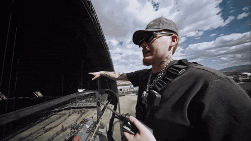 a man wearing sunglasses and a hat holds a remote control in his hand