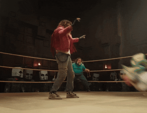 a woman in a red jacket stands in a boxing ring with a man in a green shirt