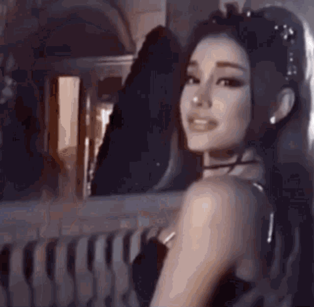 ariana grande is wearing a black dress and looking at the camera while standing on a balcony .