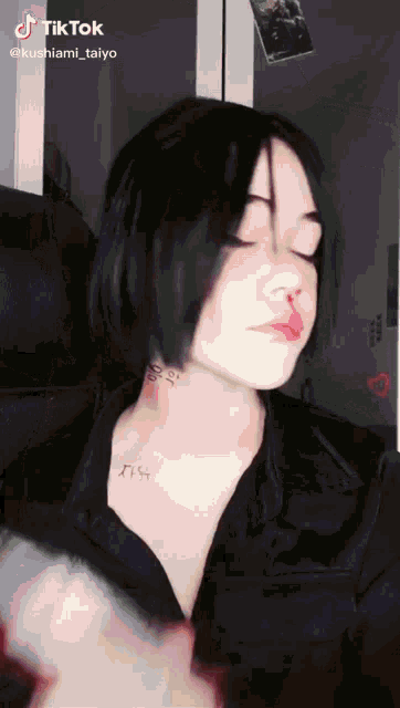 a woman with short black hair and a tattoo on her neck is sitting in a chair with her eyes closed .